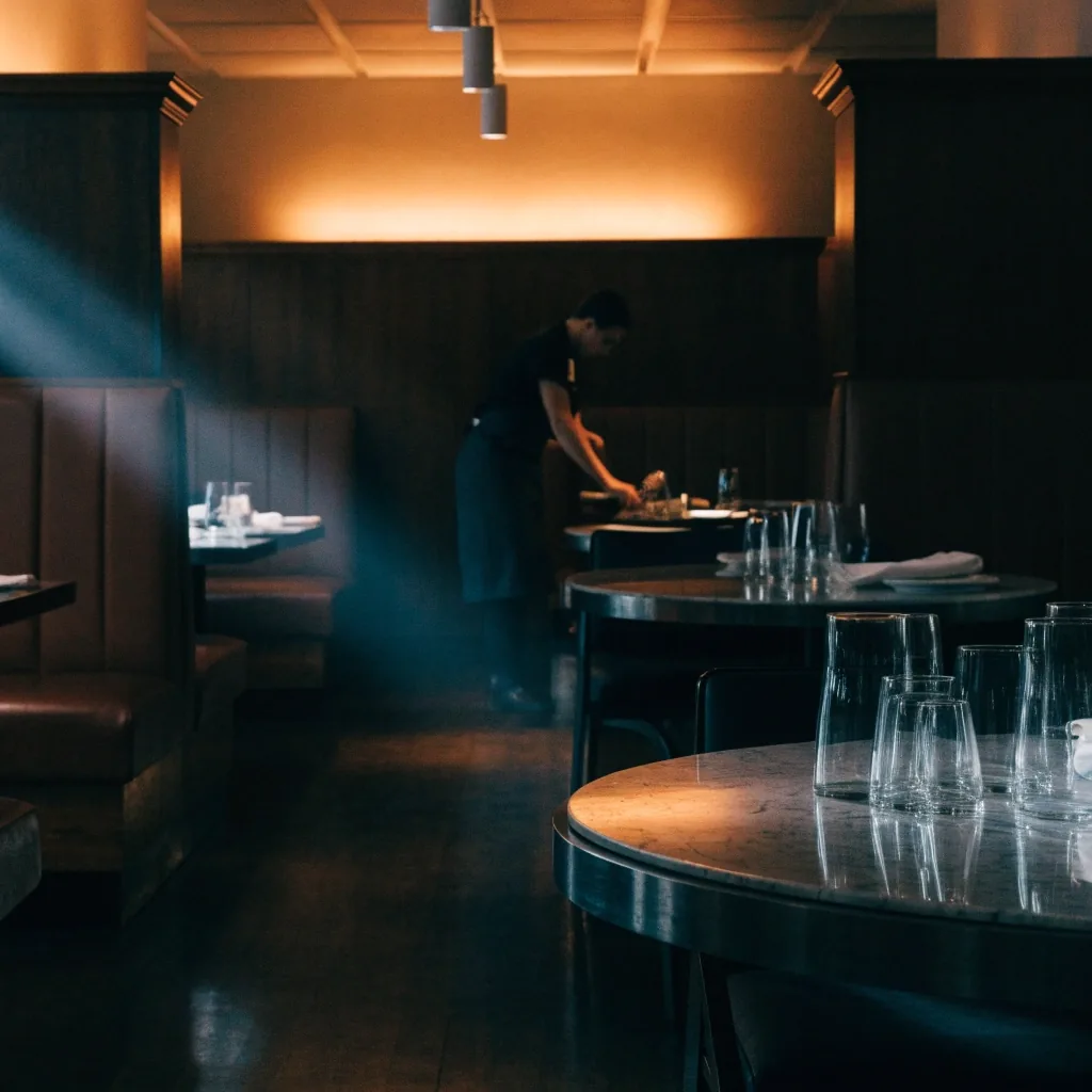 Steakhouse dining room at end of evening service, server setting a table